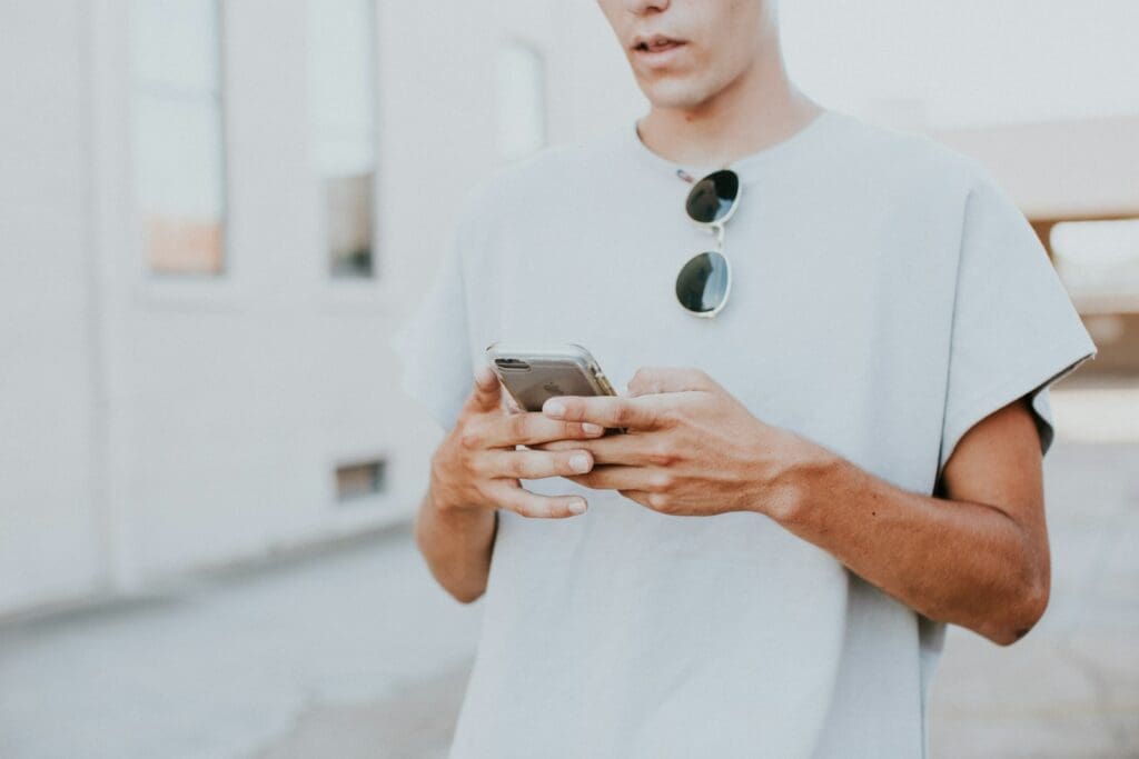 invite man in white crew-neck top using smartphone outdoors